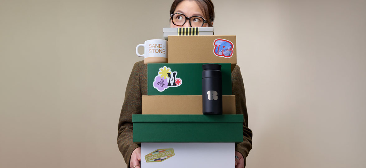Someone holding a stack of branded boxes with a branded mug and Tumbler on display