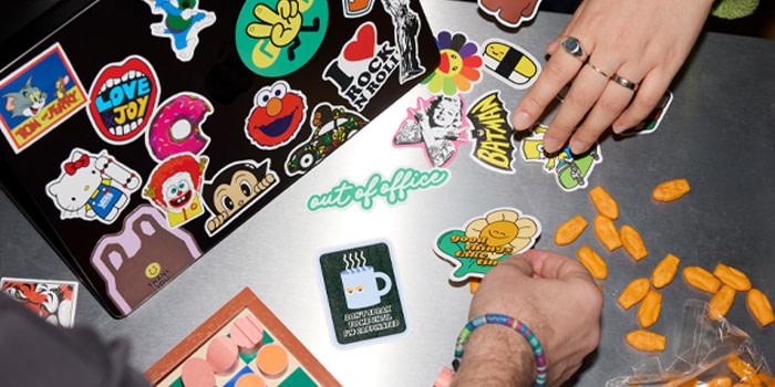 An assortment of Stickers placed on a silver surface and a black laptop lid.