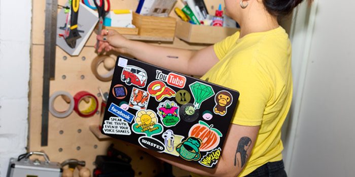 Someone holding a laptop which is decorated with Stickers.