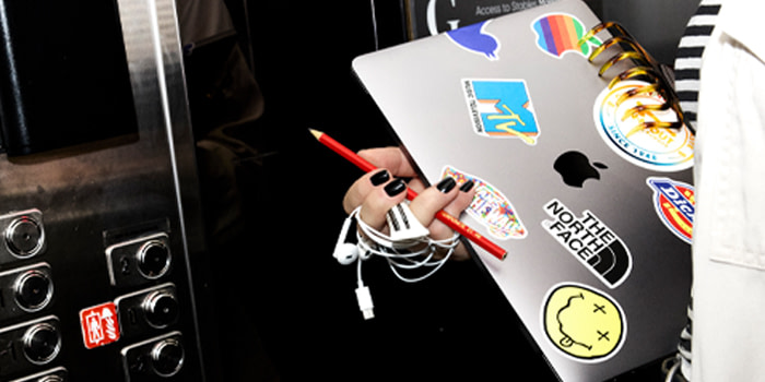 Someone holding a silver laptop which is decorated with Stickers.