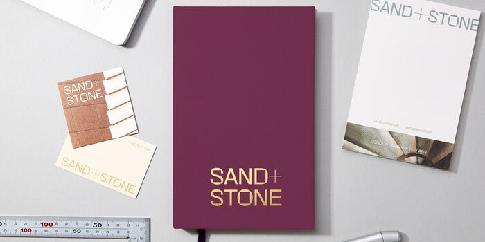 A purple Hardcover Notebook, Business Cards and a Notepad displayed on a grey desk.
