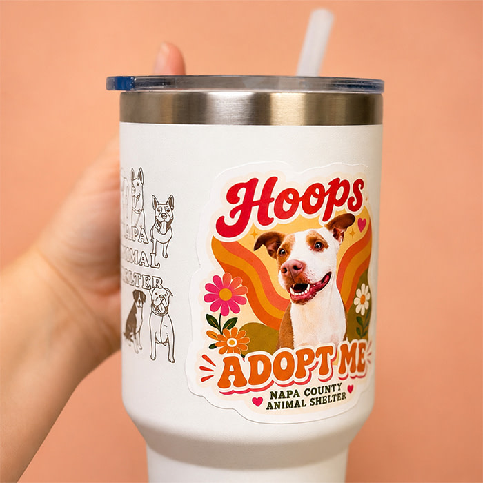 Someone holding a branded Tumbler with a Die-Cut Sticker illustration of a dog named Hoops.