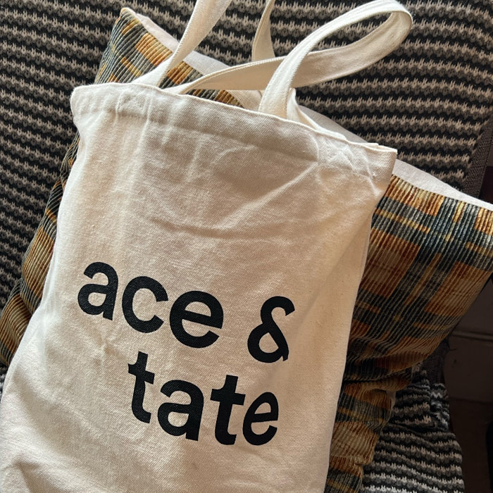 A white ace & tate tote bag placed on a couch.