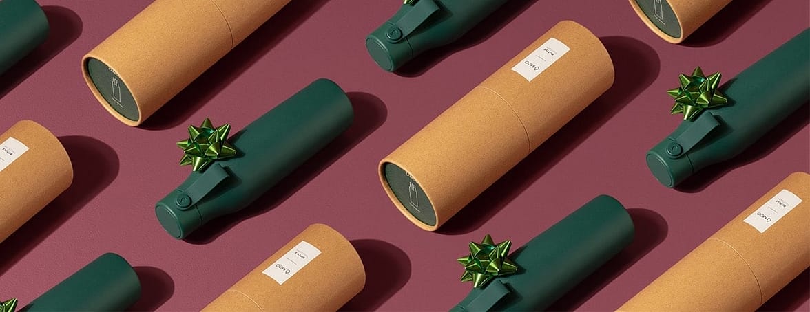 Dark green drink bottles with light green gift bows and their cardboard tube packaging laid out in lines