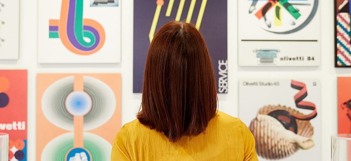 Red-haired woman seen from the back looking at a wall covered in design posters