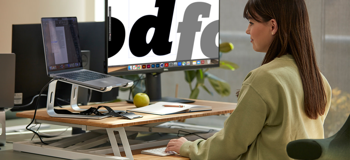 A woman sitting at a desk with two screens, designing with type