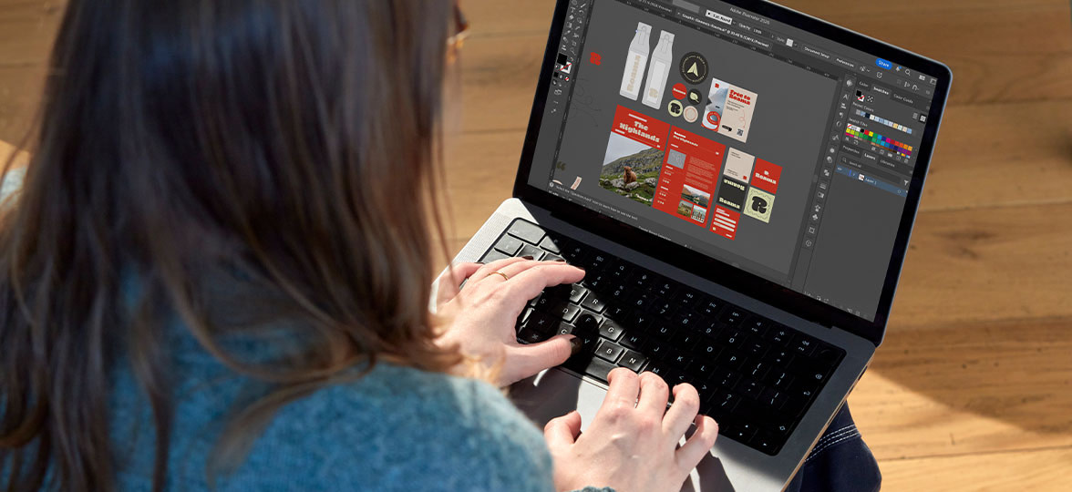 Designer working on branded merch and print designs on laptop.