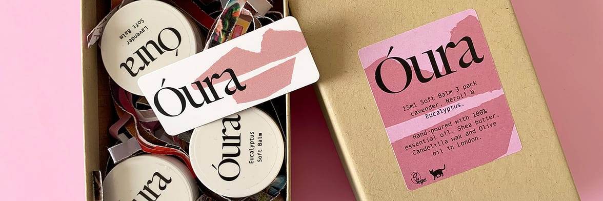 Óura's gift box with branded round stickers on balm jars, a mini card with rounded corners and a branded rectangle label to decorate the box, on a pink background