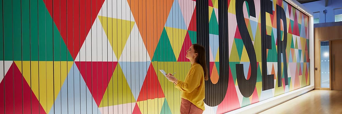Woman looking at big colorful mural with a geometric pattern design and the word user written in big letters