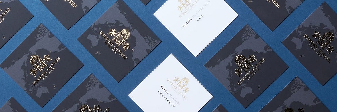 Mosaic of square black business cards with a gold foil McBride Sisters crest on the back and contact details on a white background on the front