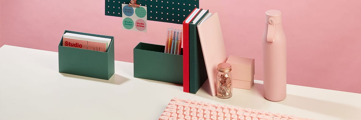 Colorful desk with notebooks, display boxes and a pink reusable water bottle