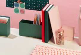 Colorful desk with notebooks, display boxes and a pink reusable water bottle