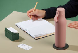 Person writing on a notrbook at their desk, with a pink water bottle
