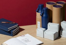 A table with newly ordered office supplies, including boxes of business cards, some water bottles, and some planners.
