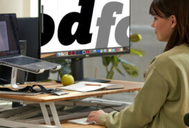 A woman sitting at a desk with two screens, designing with type