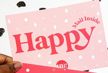 Hand holding one pastel pink happy postcard on a speckled dot background
