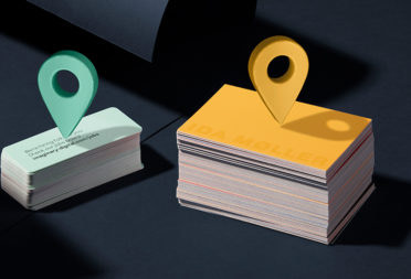 A stack of business cards and a stack of minicards with GPS location markers hovering above.