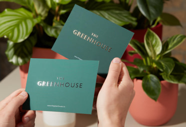 Customer holding two green Postcards with Gold Foil finish on logo.
