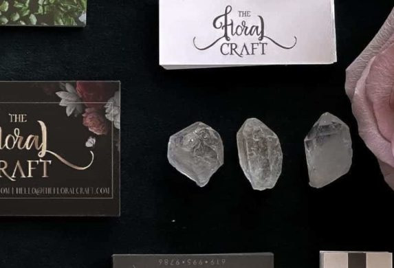 Standard business cards with floral designs, white minicards, square black business cards with a skull design, rose, butterflies and crystals on a black table
