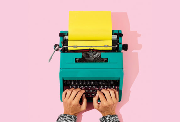 Hands typing on colorful vintage typewriter with yellow paper on pink background