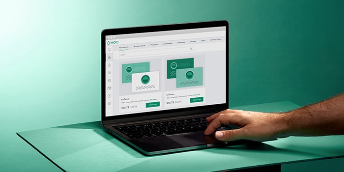 Hand typing on a laptop open to the MOO Business Services platform with available custom templates