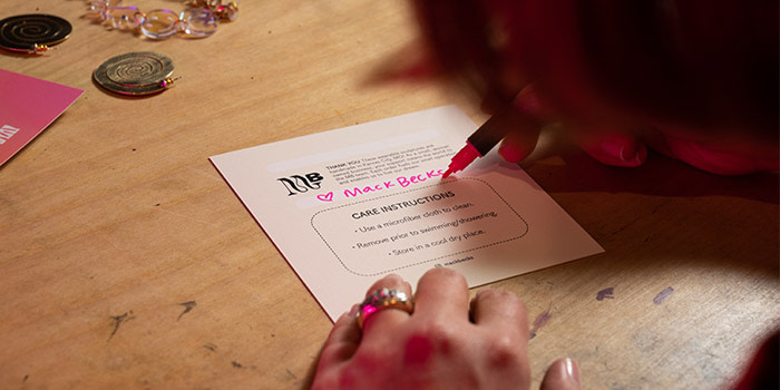 Mackenzie Becker writer a note in pink pen on a square care card by MOO