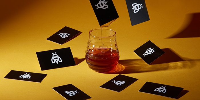 Black Industrious business cards with a white bee logo flying around a pot of honey