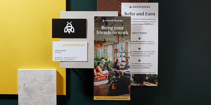 2 Industrious refer a friend rack cards front and back next to black Industrious business cards with a bee logo