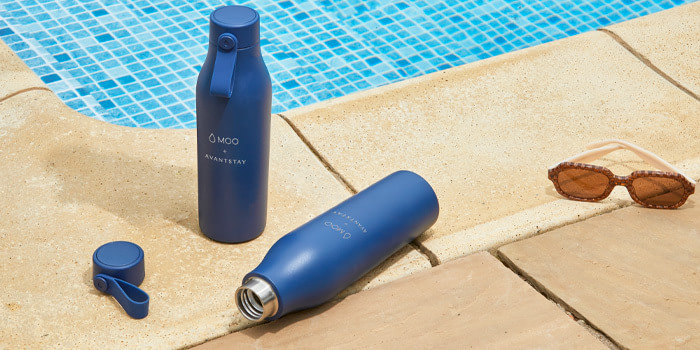 Two Branded Water Bottles and a pair of brown sunglasses placed next to a poolside.
