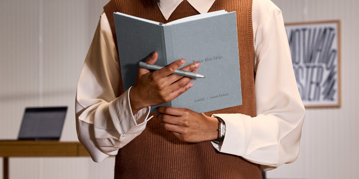 Someone holding a grey MOO Hardcover Notebook and Paper Pen in their hands.