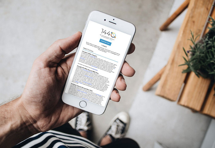 Hand holding a phone on which we can see the 1440 newsletter
