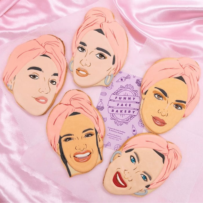 5 decorated cookies with the faces of women with a pink turban and purple Funny Face Bakery business card on a pink satin background