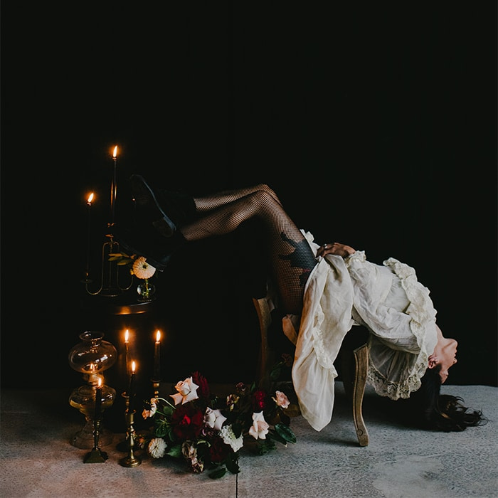 Woman in fishnets and white Victorian dress lying on a chair with her head down and her feet up.
