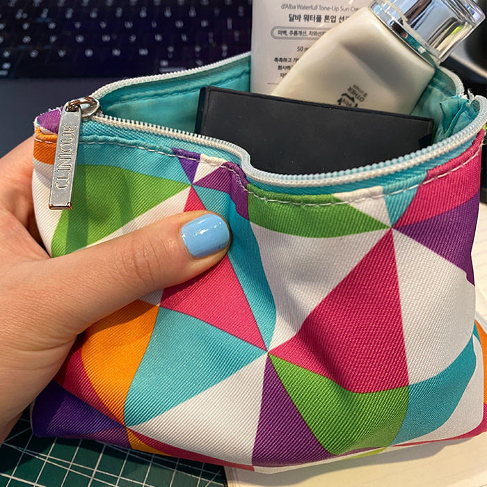 Someone holding a colorful Clinique makeup pouch with makeup inside.