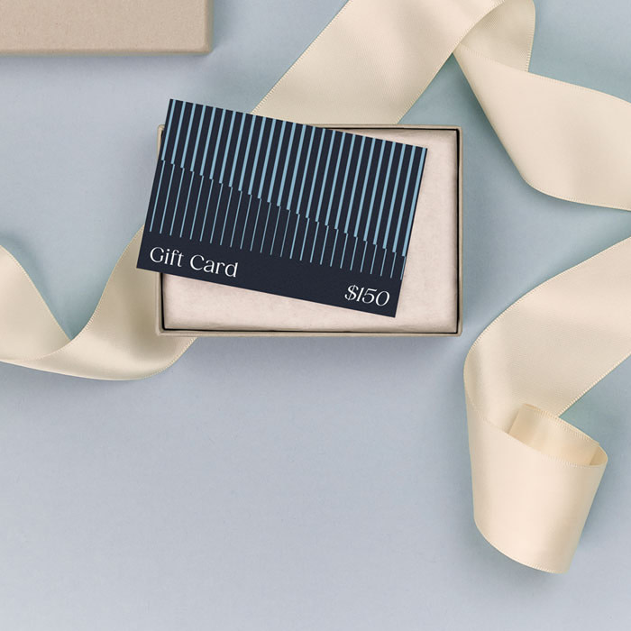 A dark blue Gift Card displayed in a cream gift box, surrounded by a cream ribbon on a light blue surface.