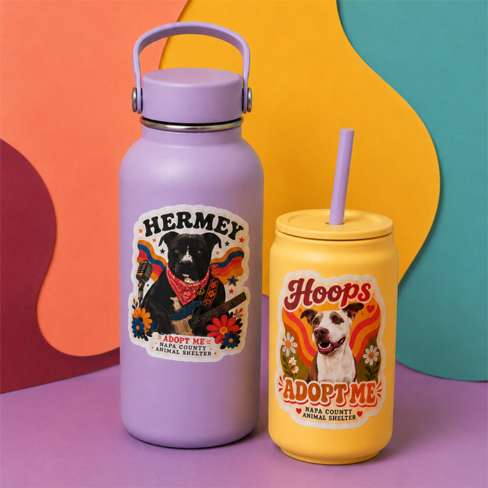 A purple water bottle and a yellow Tumbler with Die-Cut Sticker illustrations of two dogs named Hermey and Hoops placed on each of them.