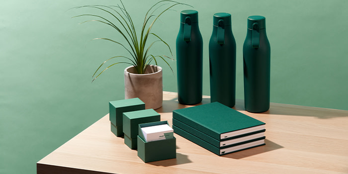 Pile of green notebooks, green display boxes and green bottles by MOO