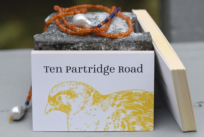 Jewelry and piles of Luxe business cards with a yellow edge and a bird illustration by Ten Partridge Road