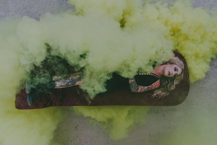 Tattooed woman lying on a vintage velvet chaise longue with green smoke all around