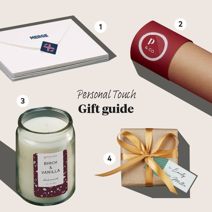Holiday-themed gift guide with a pile of custom envelopes sealed with a mini sticker, a candle with a custom label, a small gift with a mini gift tag and a custom MOO water bottle in its packaging