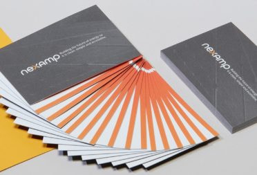 Stack of grey Nexamp business cards and Nexamp cotton business cards fanned out so we see an orange line at the bottom of the design