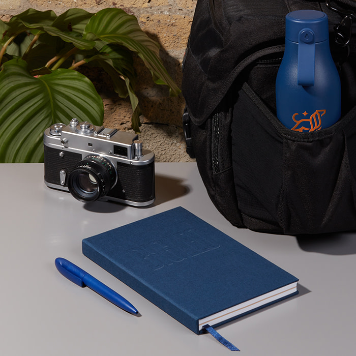 Camera, custom notebook and custom water bittle in a camera backpack