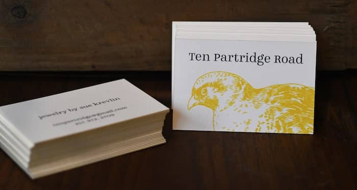 Pile of Luxe business cards with a yellow edge and a bird illustration by Ten Partridge Road