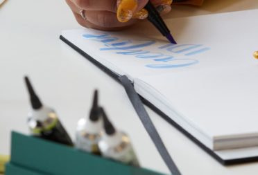 Someone with painted nails doing calligraphy in a notebook