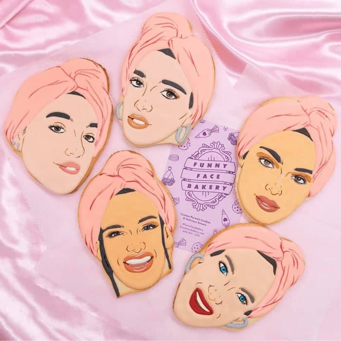 5 decorated cookies with the faces of women with a pink turban and purple Funny Face Bakery business card on a pink satin background
