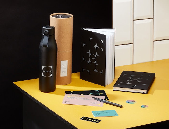 Black water bottle, custom black notebooks and print materials on a yellow table