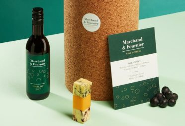 Mini bottle of wine with a green label, block of cheese, big cork pedestal with a round sticker, grape and big green postcard for a wine and cheese business