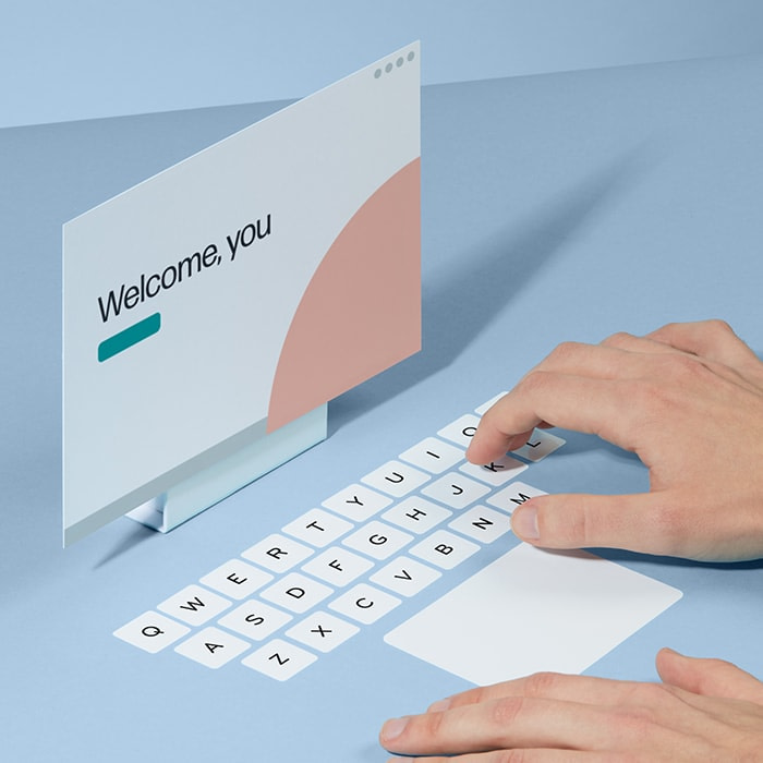 Hand typing on a fake keyboard made of mini square stickers in front of a welcome screen made of a postcard