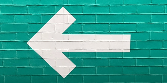 White arrow pointing left painted on a green brick wall