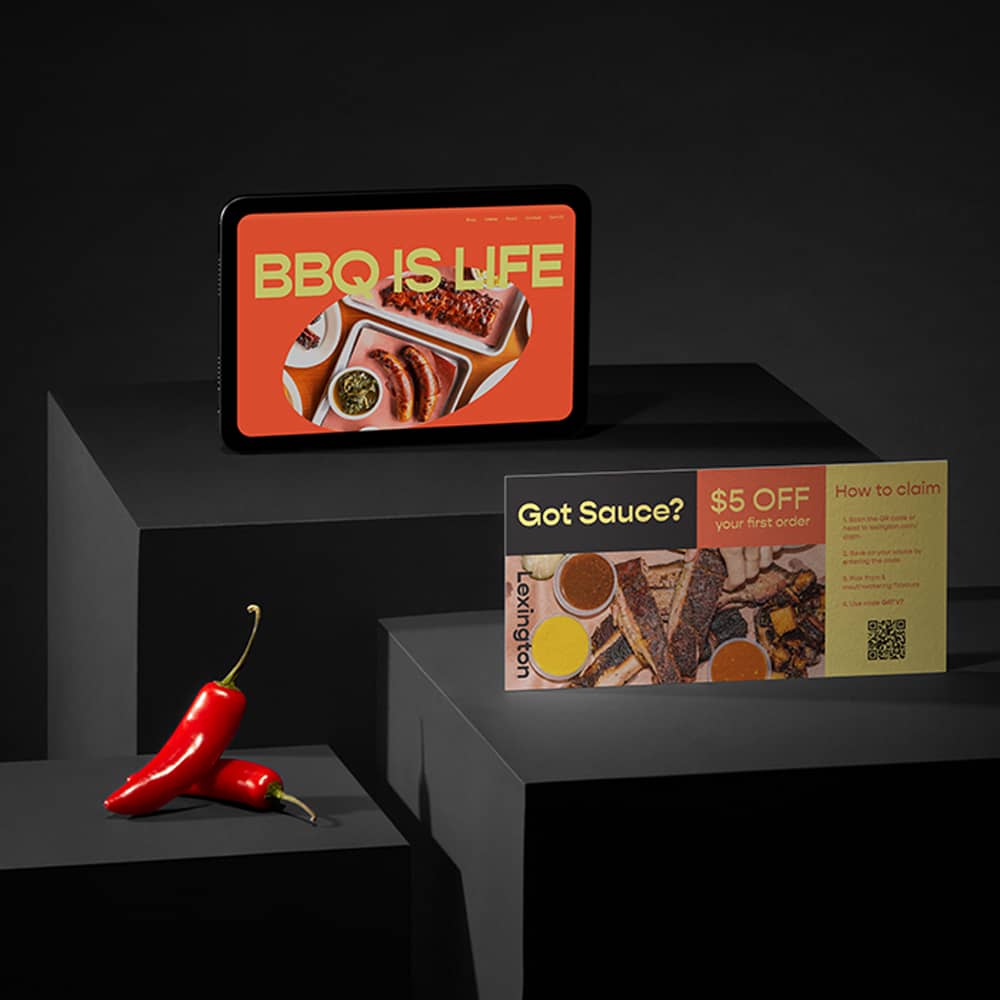 A BBQ brand is showcased on a tablet with their Squarespace website and on flyers including a QR code. Next to them sits some chili peppers.
